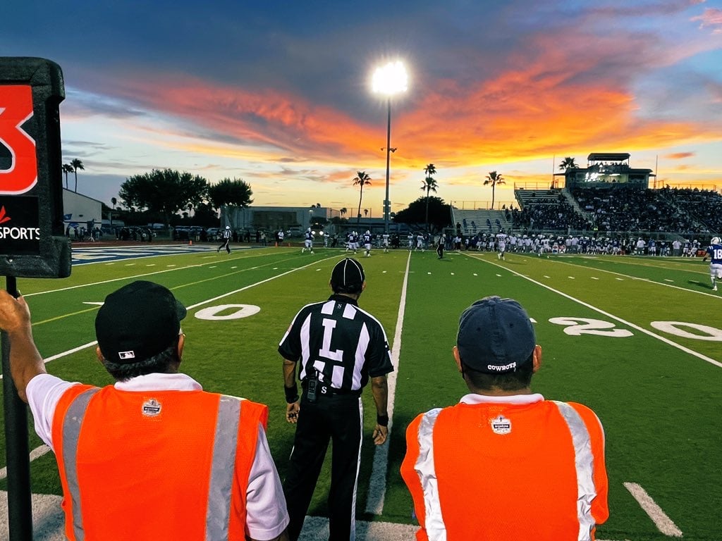 Sunset football game photo with referee and line staff.