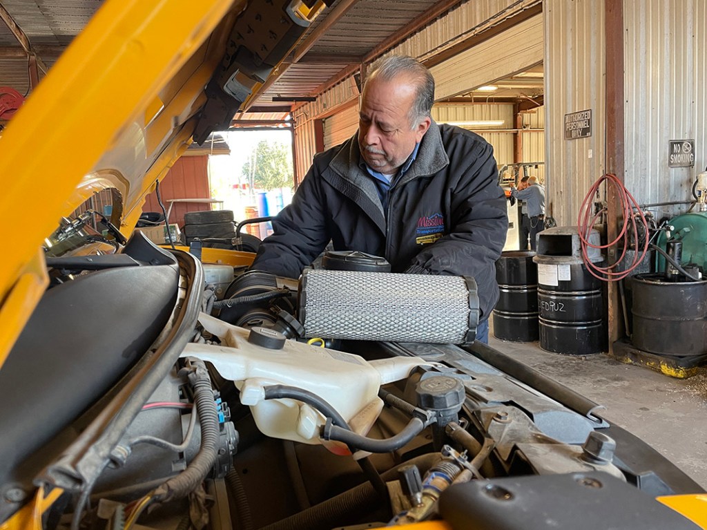 Transportation Department mechanic working on motor of a school bus. 